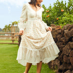 Woman in a white lace dress standing outdoors near a stone wall with greenery in the background