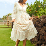Woman in a white lace dress standing outdoors near a stone wall with greenery in the background