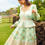 Woman in a light green floral dress standing outdoors with greenery in the background