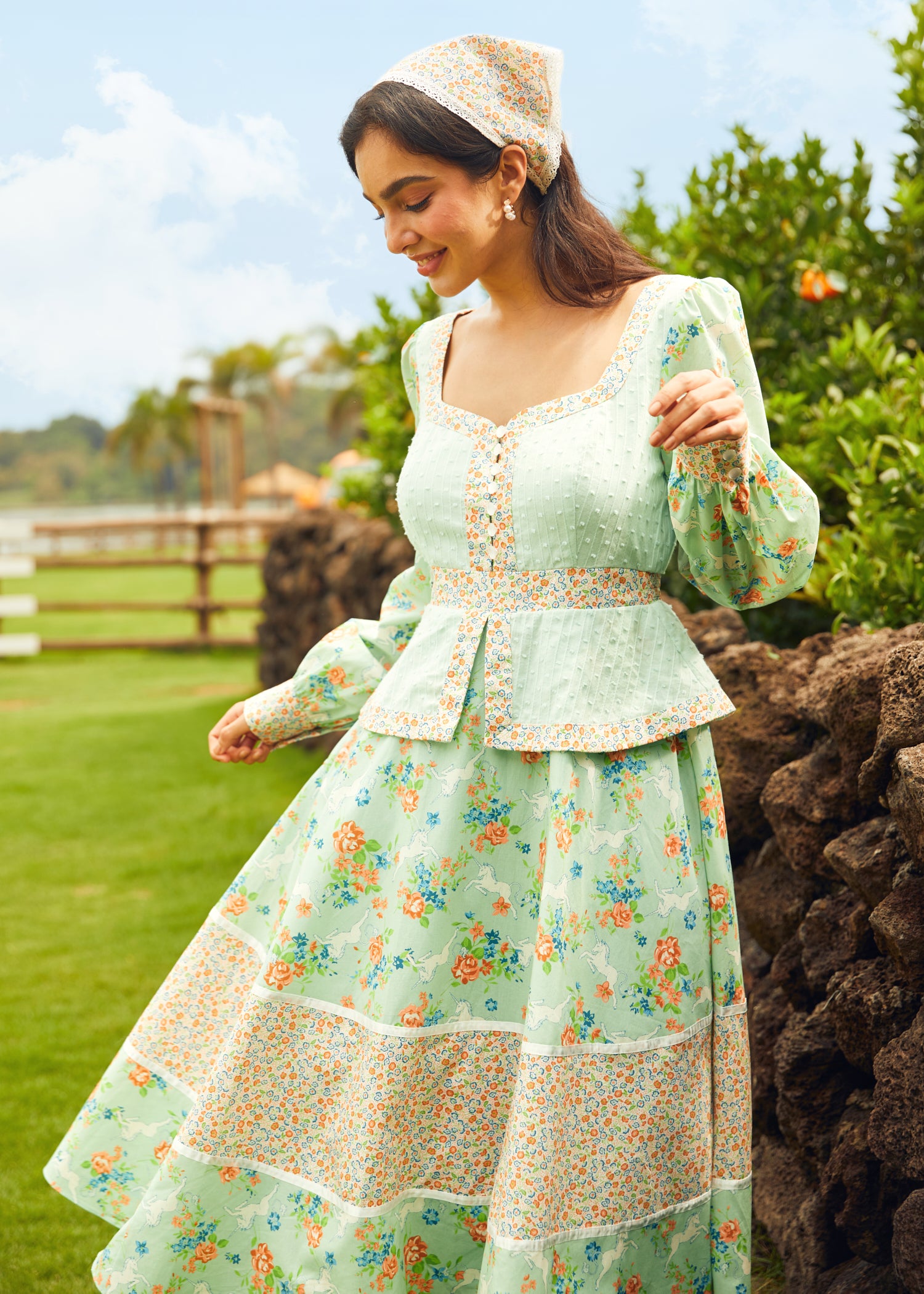 Woman in a light green floral dress standing outdoors with greenery in the background