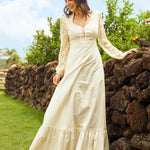 Woman in a white dress standing outdoors near a stone wall with greenery in the background