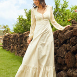 Woman in a white dress standing outdoors near a stone wall with greenery in the background