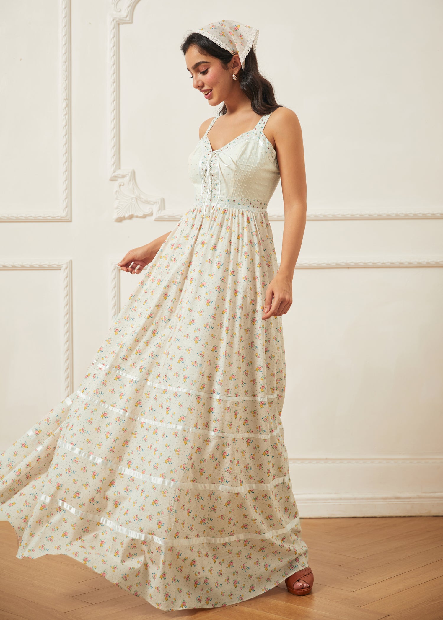 Woman wearing a long, light-colored dress with a subtle pattern against a white wall.