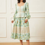 Woman wearing a light green dress with floral pattern against a white wall.