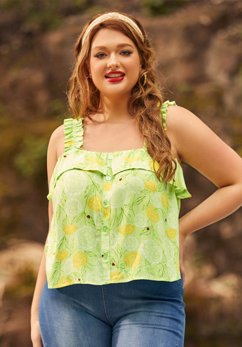 A woman wearing a light green, lemon-patterned blouse with ruffled spaghetti straps and a button-down front, paired with blue jeans.