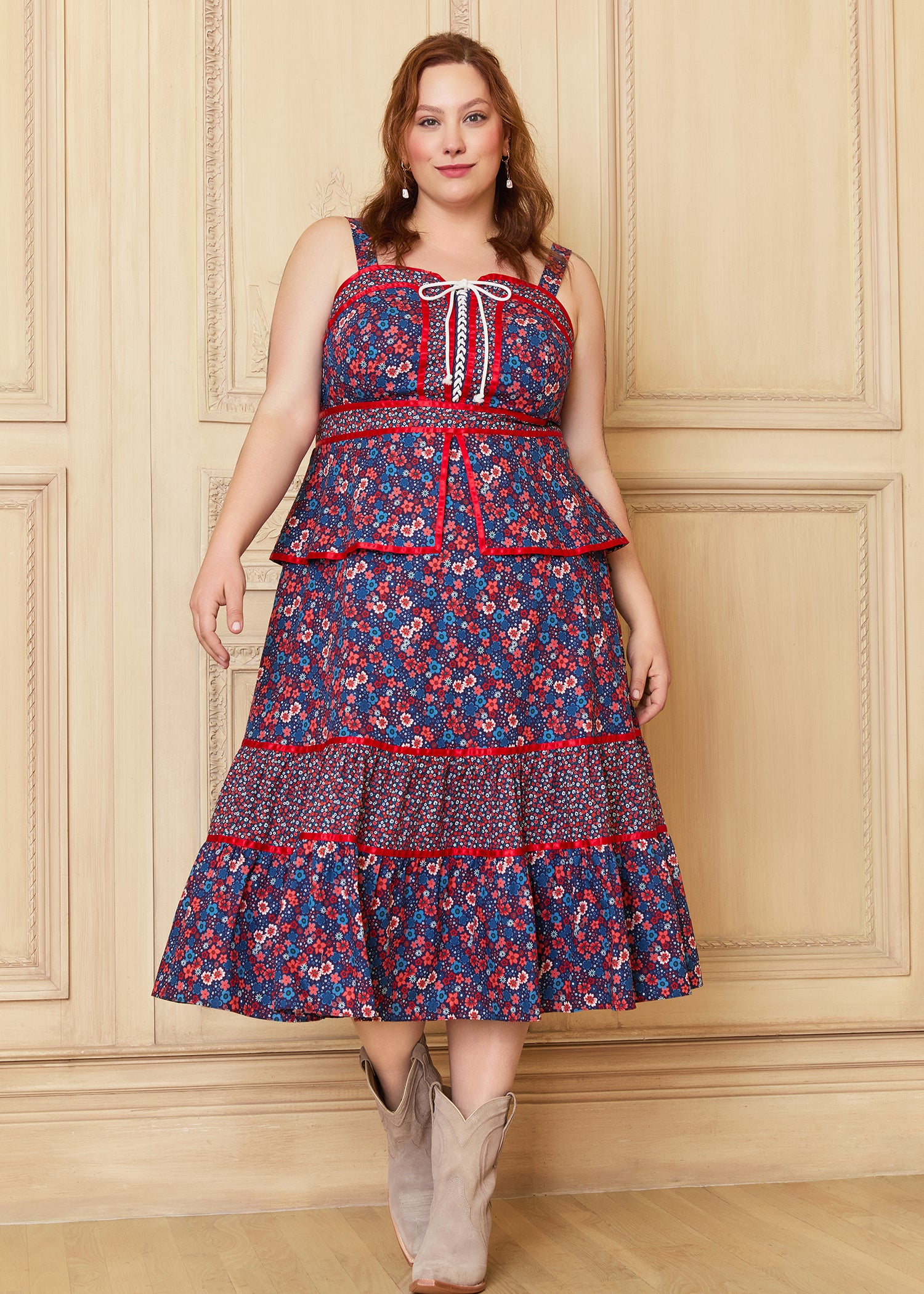 A woman models the GUNNE SAX for ModCloth Grace Peplum Midi Dress, featuring a floral pattern with red accents, a peplum bodice, and a fully lined, tiered skirt.