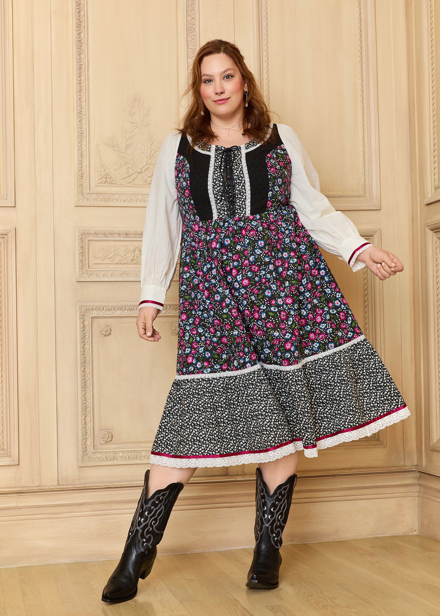 A woman modeling a GUNNE SAX for ModCloth Madilyn Midi Dress with floral prints, featuring a corset-inspired bodice, long sleeves, and black boots.