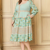 Woman wearing a mint green dress with floral patterns against a wooden paneled wall.