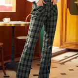 A person standing in a cafe wearing high-waisted 70's inspired green plaid wide-leg trousers with pockets.