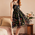 Woman wearing a sleeveless fit-and-flare party dress with sheer embroidered floral mesh and full skirt.