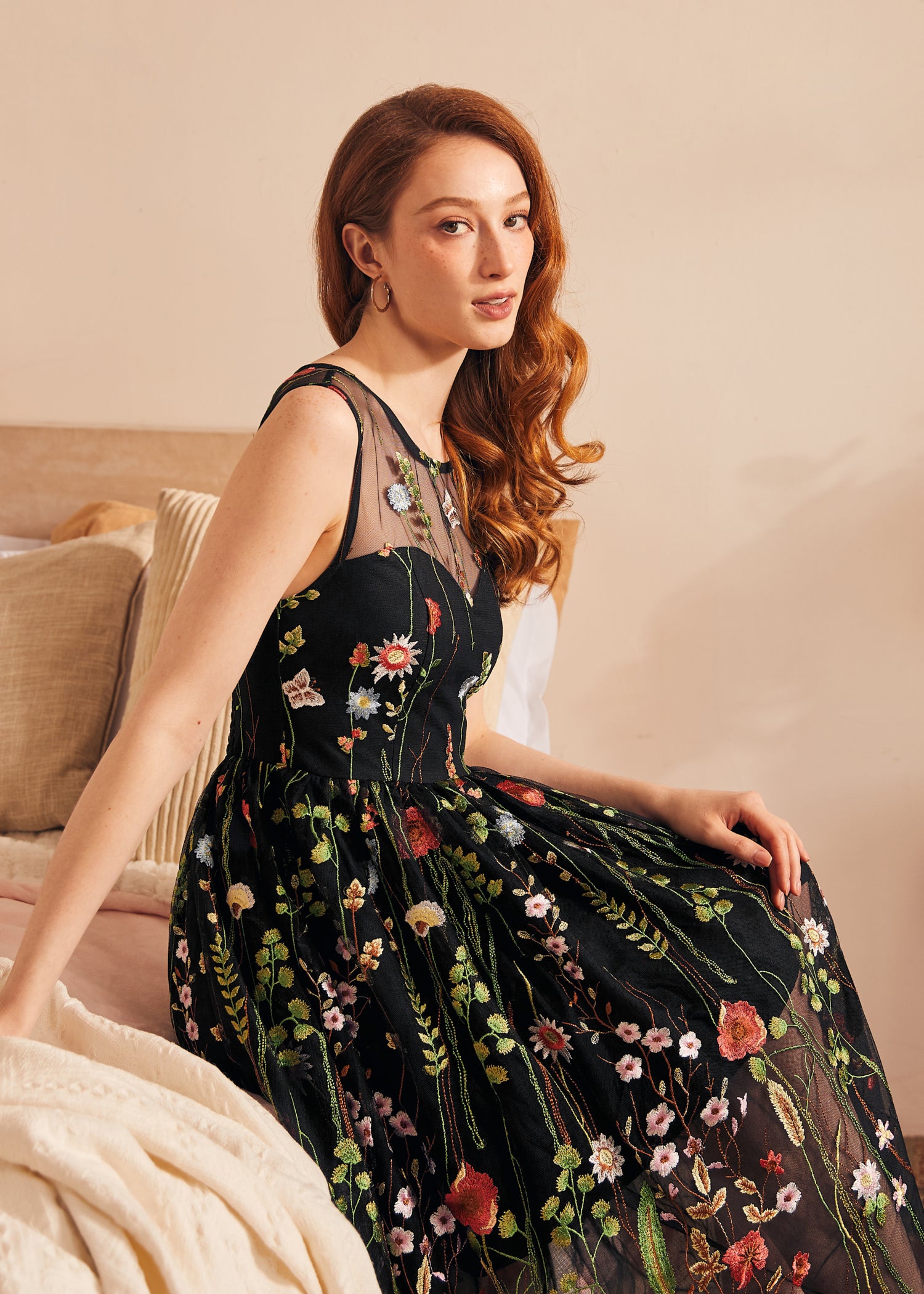 Woman seated wearing a vintage-inspired black embroidered mesh dress with floral tulle overlay.
