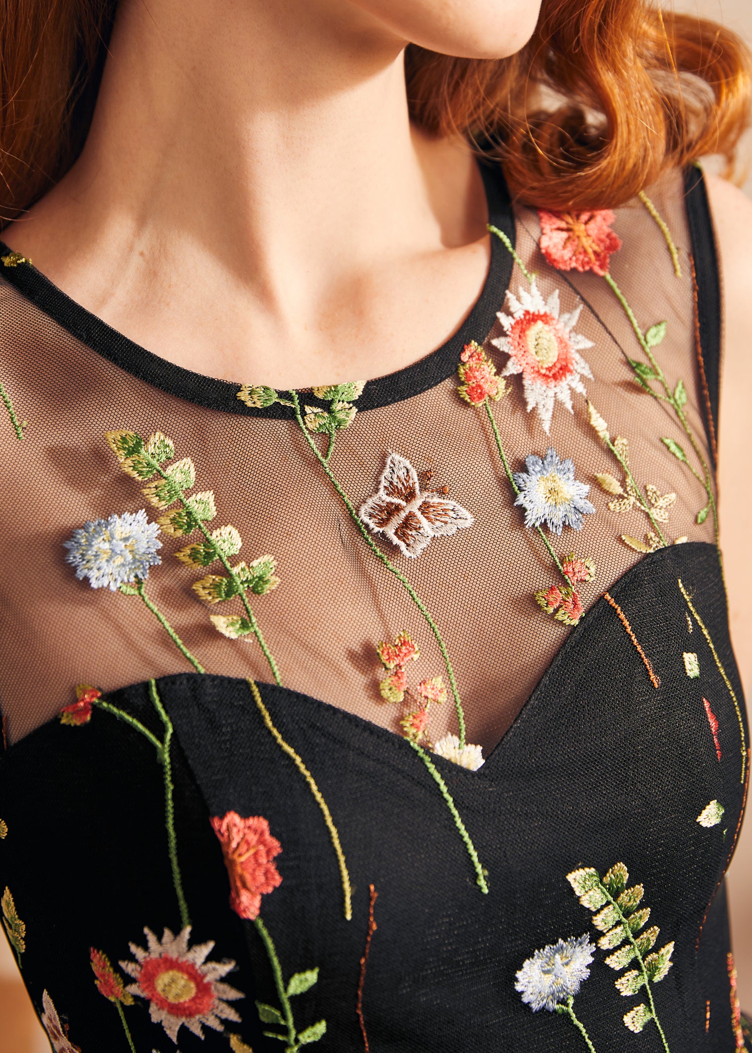 Close-up of the illusion mesh yoke with colorful floral embroidery and embroidered butterfly details on a black party dress.