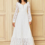Woman wearing a white lace dress against a wooden paneled wall.