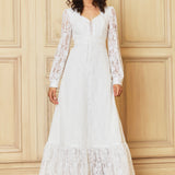 Woman wearing a white lace dress against a wooden paneled wall.