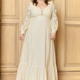 A plus-size model wearing a high collar corselette maxi dress in beige, featuring long sleeves with lace detailing and a ruffled hem.