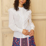 A woman modeling a white long-sleeve ruffle top with a round neckline, paired with a multicolored floral skirt.