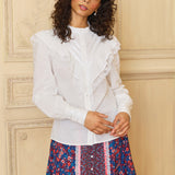 A woman modeling a white long-sleeve ruffle top with a round neckline, paired with a multicolored floral skirt.