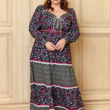 A woman standing in a room with a plain background, wearing a long sleeve, floral maxi dress with a sweetheart neckline and lace trims.