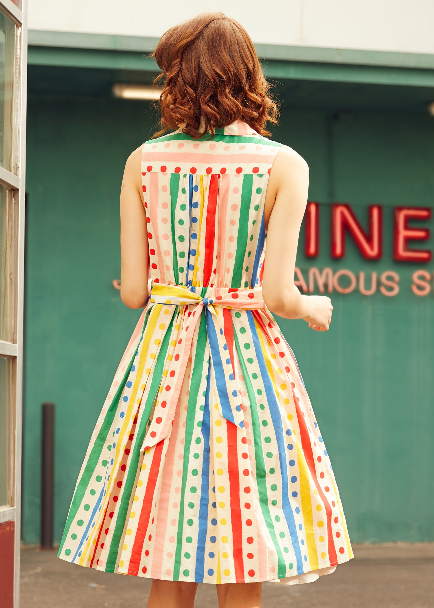 Back view of the Rainbow Carousel sleeveless fit-and-flare dress with rainbow stripe and polka dot print.