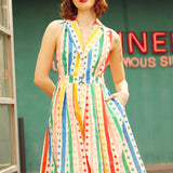 Woman wearing the Rainbow Carousel sleeveless cotton dress with pockets and colorful retro-inspired print.