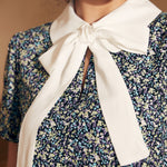 Close-up of a woman wearing a floral blouse with a white collar and bow.