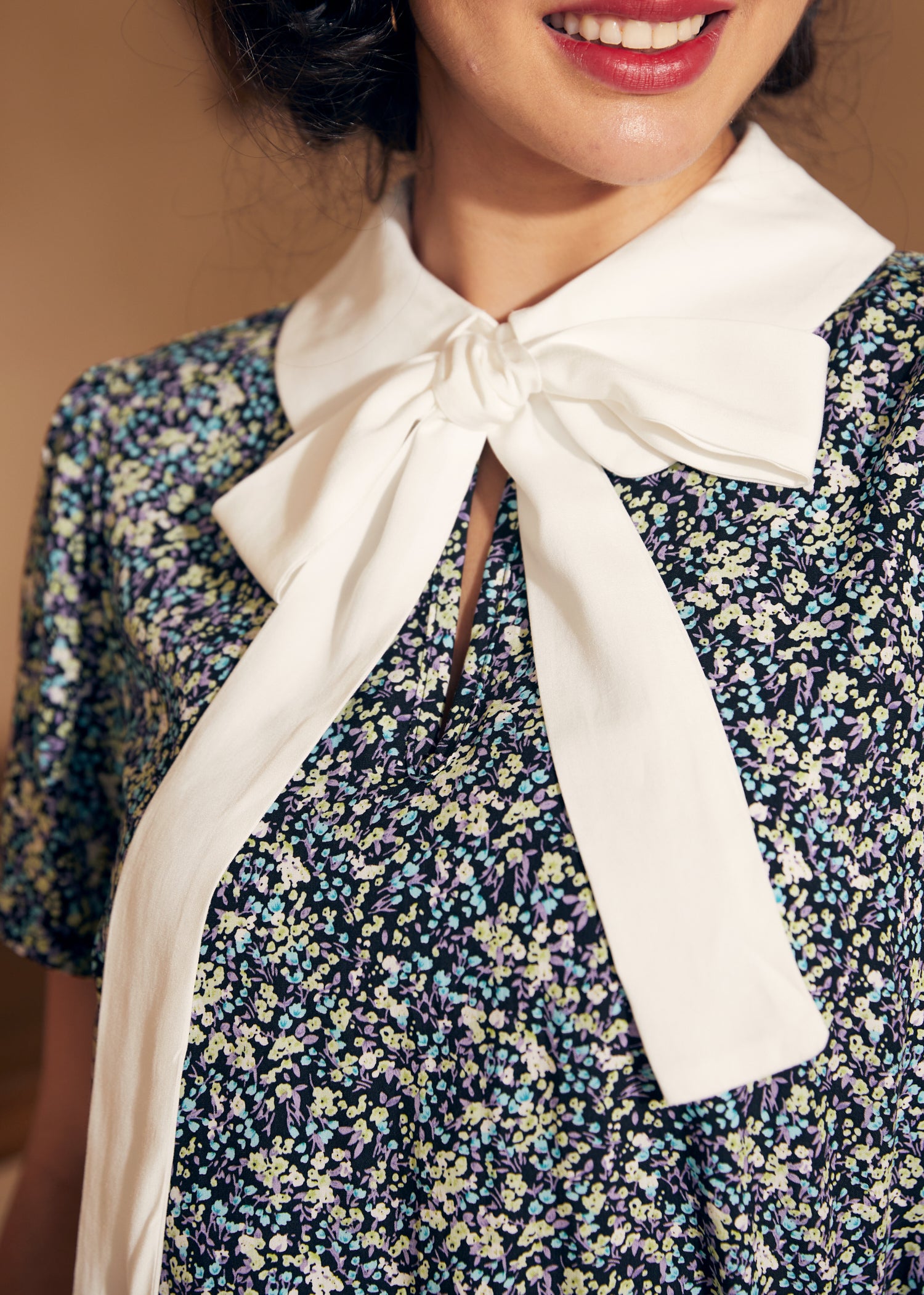 Close-up of a woman wearing a floral blouse with a white collar and bow.