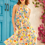 Woman wearing a colorful fruit pattern dress in front of a blue door and pink flowers.