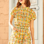 Woman wearing a yellow plaid dress standing against a textured wall.