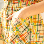 Close-up of a sleeveless romper with a checkered pattern featuring lemon print, designed with a smocked waistband.