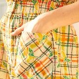 Close-up of a sleeveless romper with a checkered pattern featuring lemon print, designed with a smocked waistband.