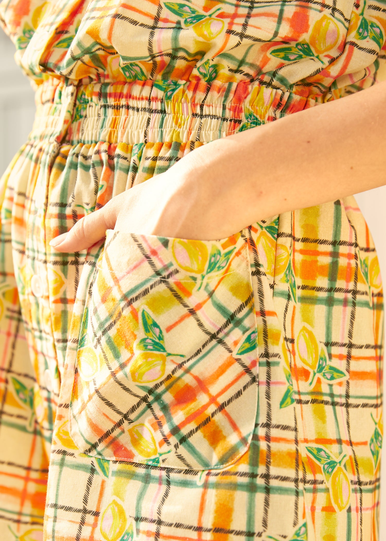 Close-up of a sleeveless romper with a checkered pattern featuring lemon print, designed with a smocked waistband.