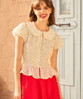 Woman wearing a polka dot blouse and red skirt standing in front of a white door.