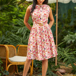 Woman in a floral dress standing outdoors with greenery and a white umbrella in the background