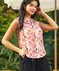 Woman wearing a floral sleeveless top and black pants outdoors.