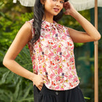 Woman wearing a floral sleeveless top and black pants outdoors.
