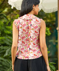 Back view of woman wearing a sleeveless floral top with a blurred green background