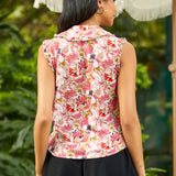 Back view of woman wearing a sleeveless floral top with a blurred green background