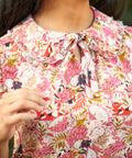 Close-up of a person wearing a floral patterned blouse with dragonfruit and hidden cats, a peter pan collar with ruffle trim, and a bow.