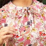 Close-up of a person wearing a floral patterned blouse with dragonfruit and hidden cats, a peter pan collar with ruffle trim, and a bow.