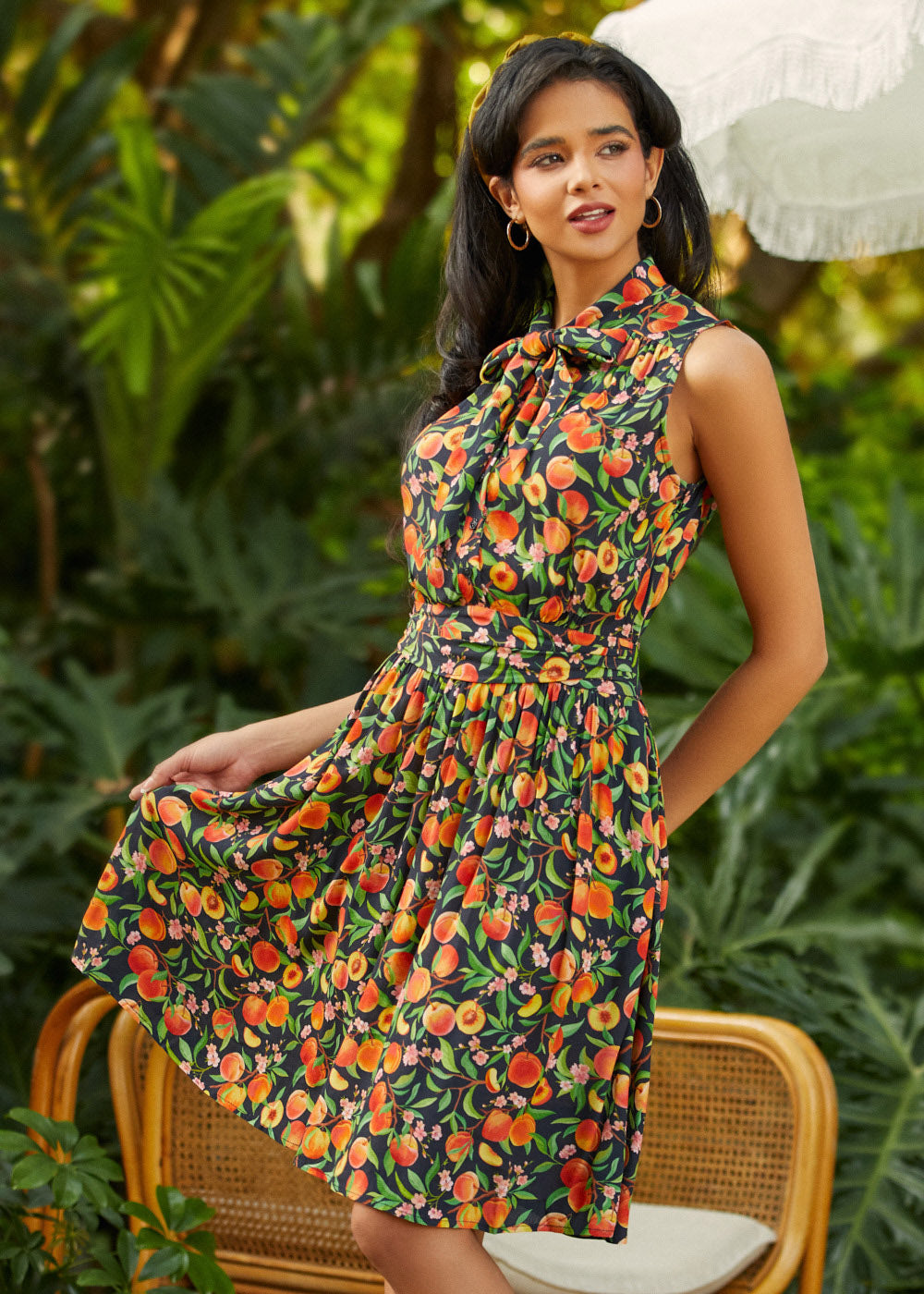Model wearing peach print bow neck fit and flare dress with sleeveless silhouette