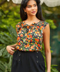 Woman wearing a sleeveless peach print top with a blurred green background