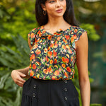 Woman wearing a sleeveless peach print top with a blurred green background