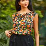 Woman wearing a sleeveless peach print top with a blurred green background