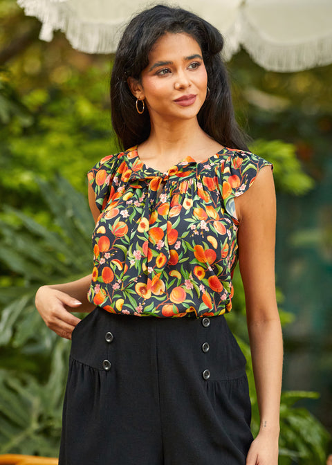 Woman wearing a sleeveless peach print top with a blurred green background