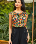 Woman wearing a floral top and black shorts standing outdoors with greenery in the background