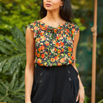Woman wearing a floral top and black shorts standing outdoors with greenery in the background