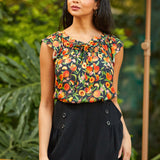 Woman wearing a floral top and black shorts standing outdoors with greenery in the background