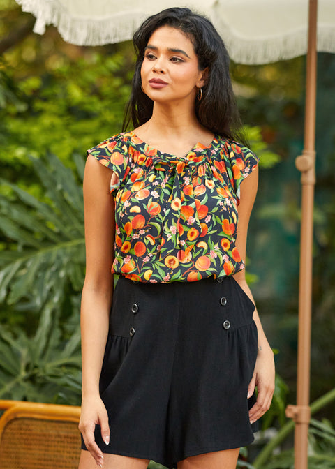 Woman wearing a floral top and black shorts standing outdoors with greenery in the background