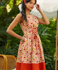 Woman wearing a patterned dress with a red bottom section, standing outdoors with greenery in the background.