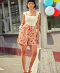 Woman in a white top and high waist red striped shorts standing outdoors with balloons in the background